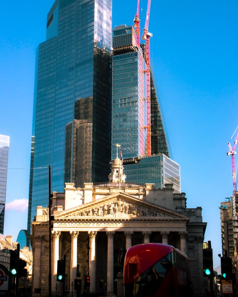 a red double decker bus driving past a tall building