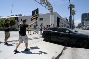 Participants in SAG-AFTRA strike wave signs and protest in a city setting.