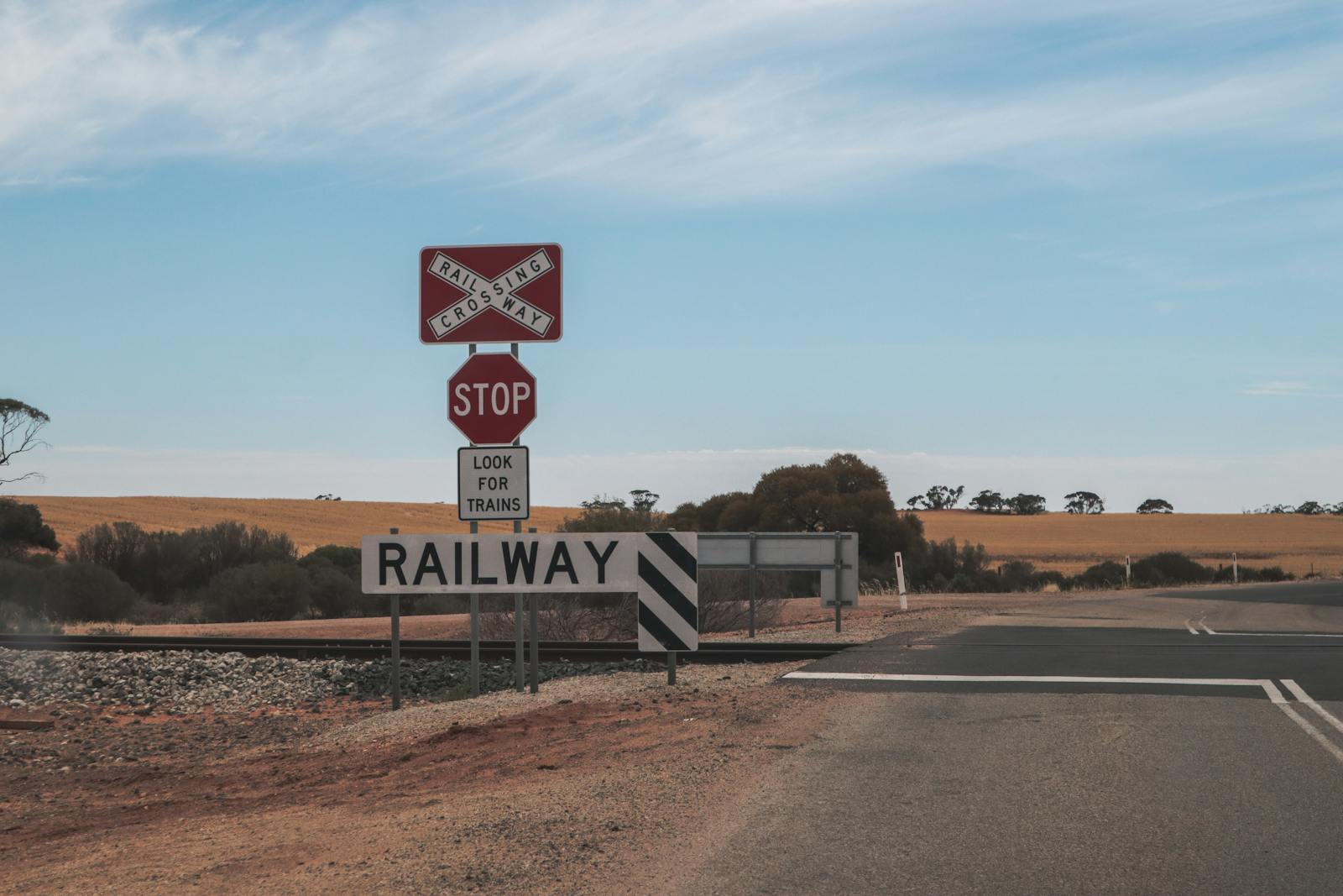 Railway crossing in a rural desert setting with clear skies and open road.
