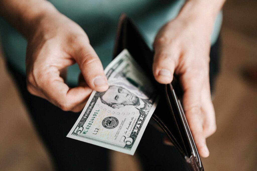 A person taking a five dollar bill from a wallet symbolizing personal finance and budget management.