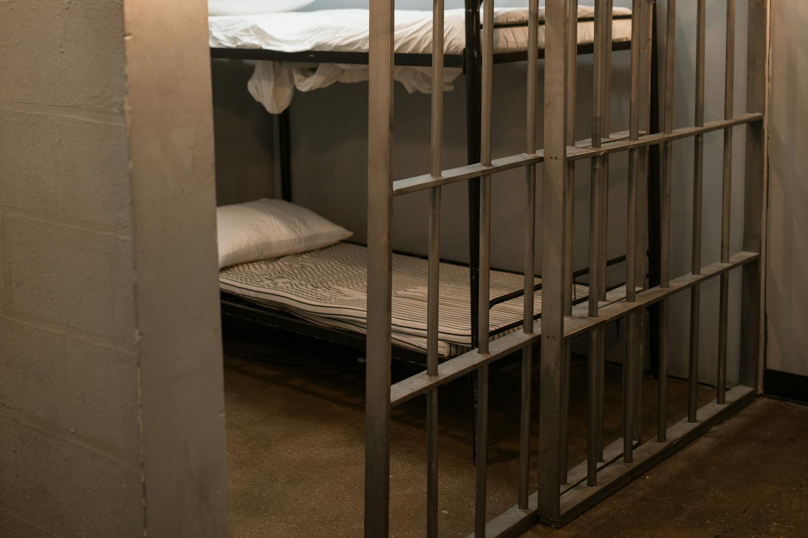 A prison cell featuring a metal bunk bed and striped sheets.