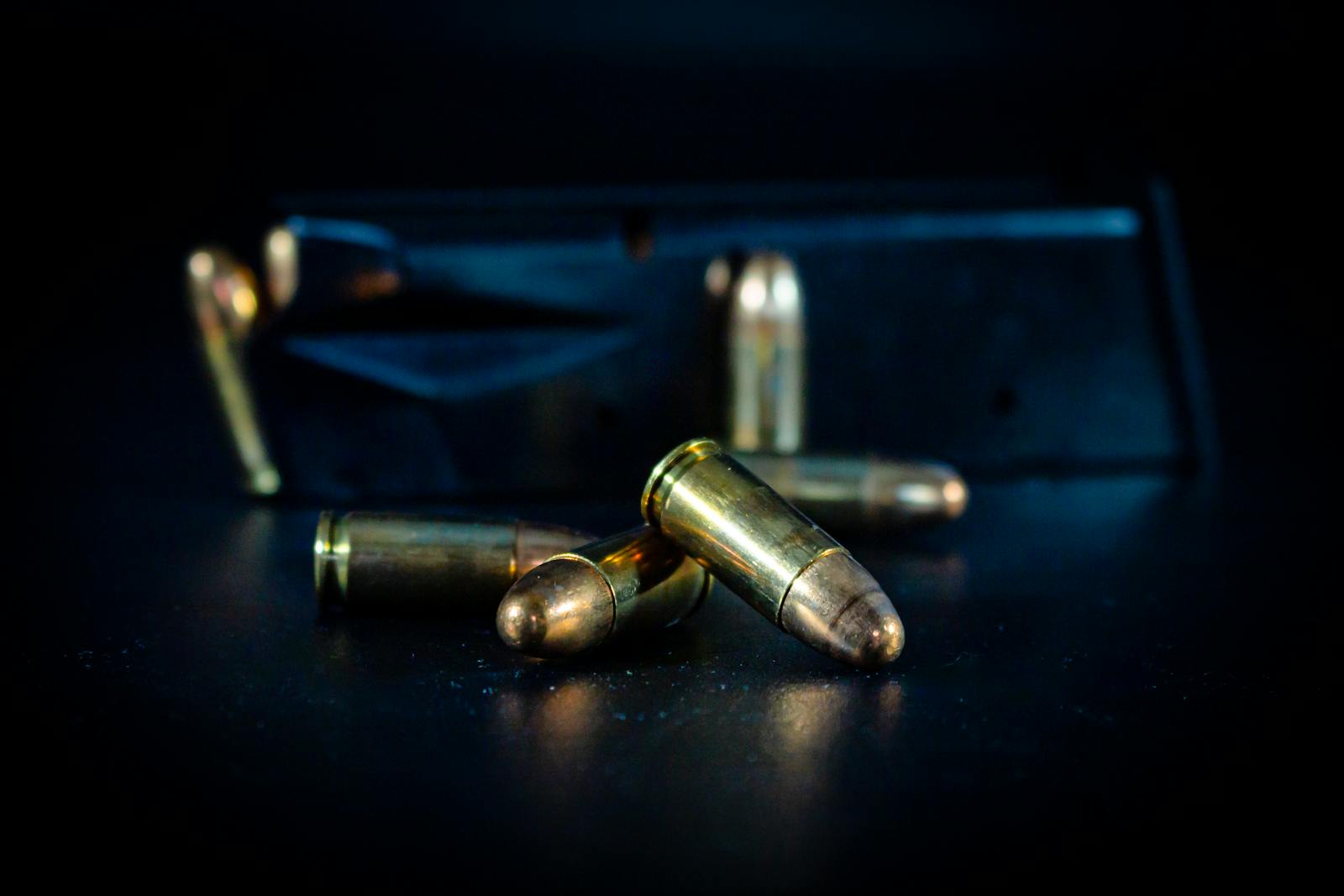 A macro shot of bullets and a gun magazine on a dark surface, highlighting the metallic texture.