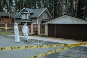 Crime scene investigators in protective suits examining evidence at a suburban house with yellow tape.