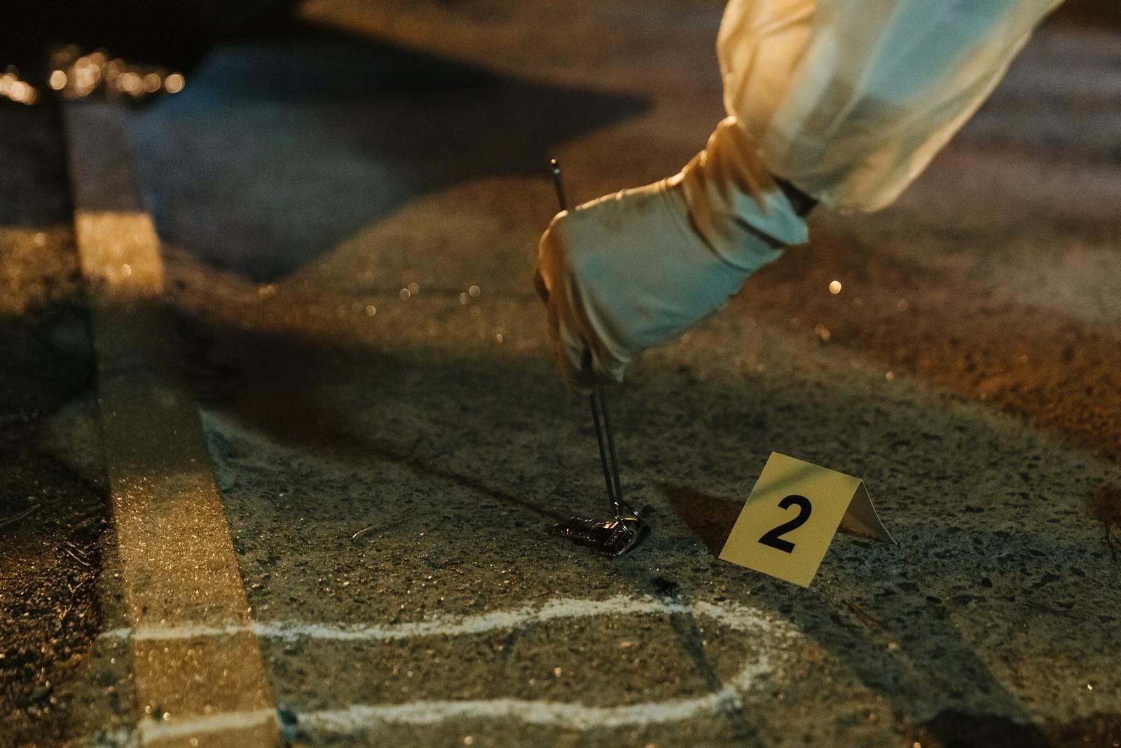 Close-up of a forensic investigator collecting evidence at a night crime scene with gloved hands.