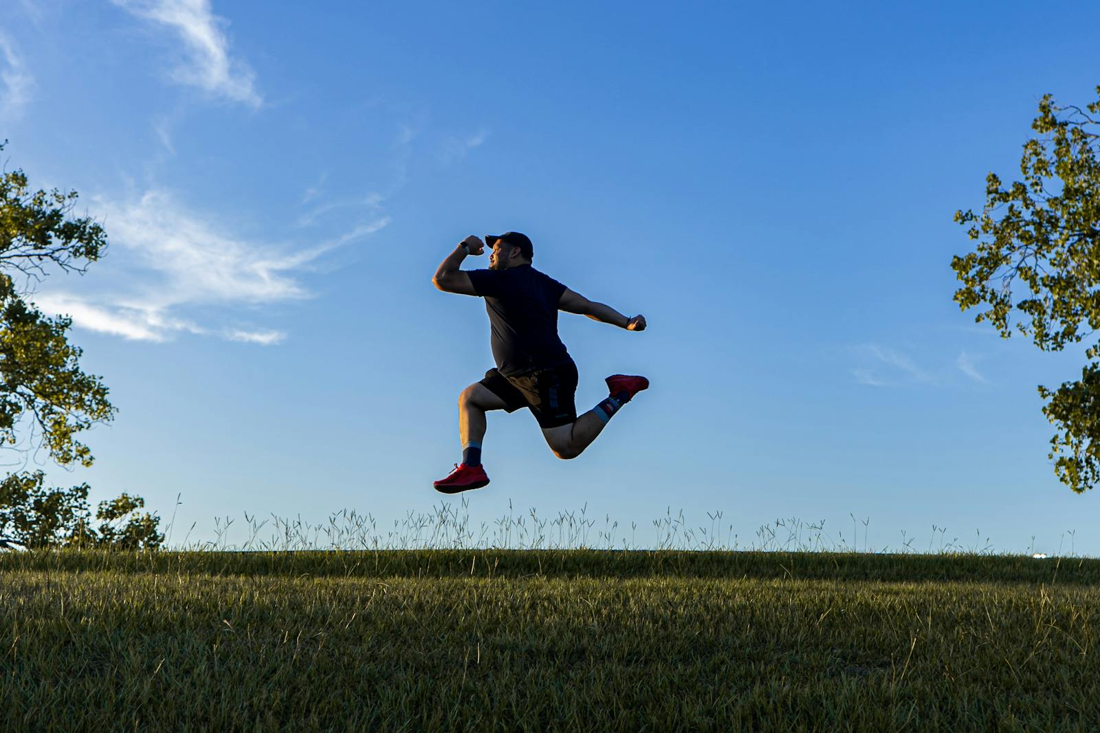 A man jumping in a Houston park field during the day with a clear blue sky.