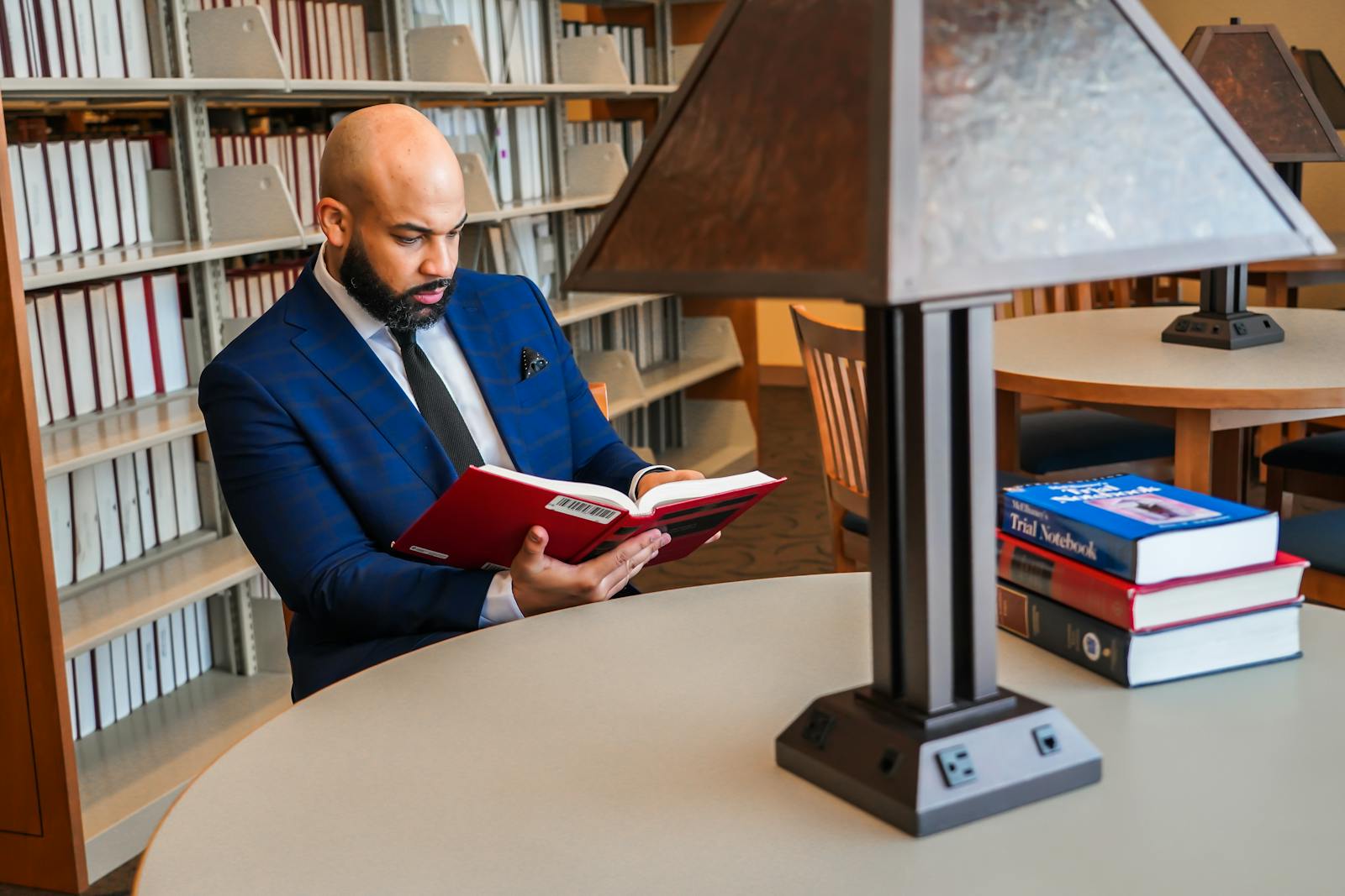 A man in a library reading a book, showcasing focus and study in a modern setting.