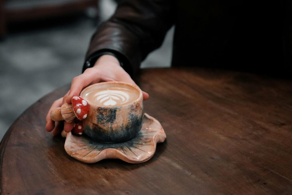 Close-up of a unique ceramic coffee cup with latte art, held by a hand on a wooden table.