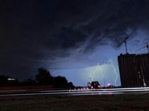 Striking lightning illuminates the night city skyline against a backdrop of dark clouds and urban structures.