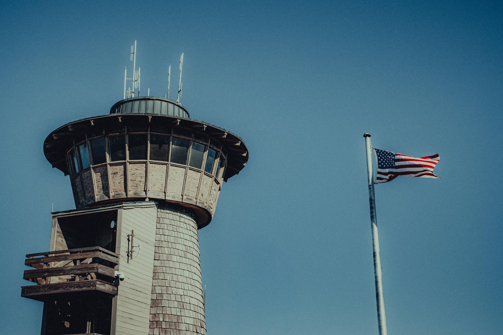 Vintage air control tower with an American flag against a clear blue sky.