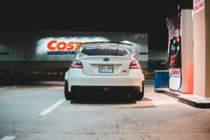 Contemporary white car parked near pump on fuel station at night in city