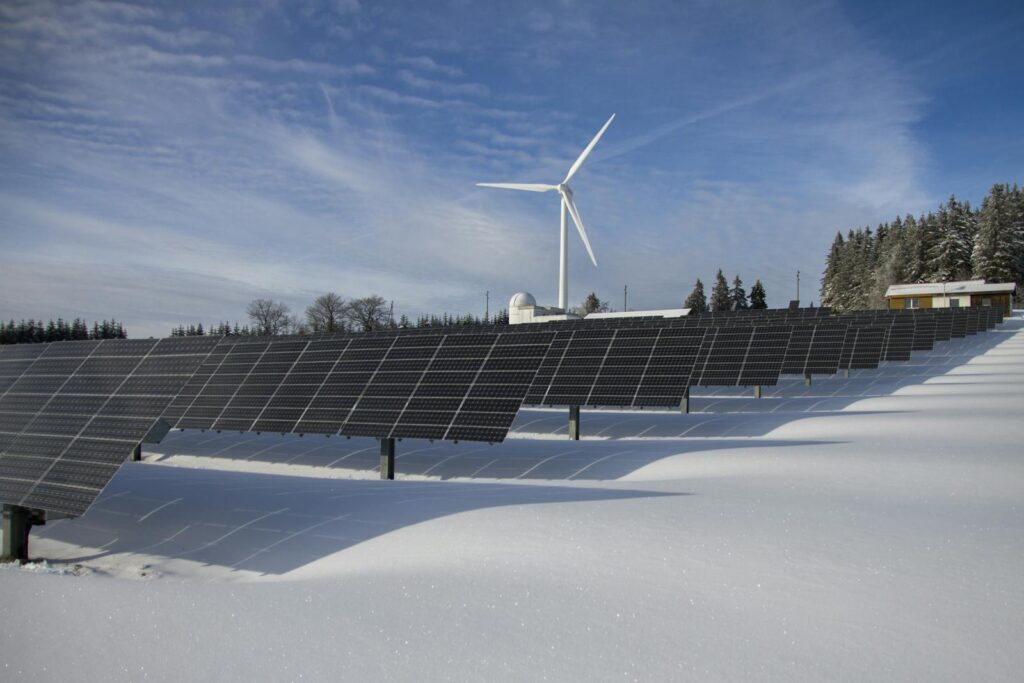 Solar panels and wind turbine in a snowy landscape, showcasing renewable energy sources.