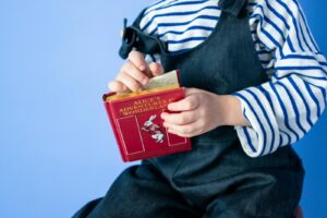 Young child in striped shirt holding red Alice in Wonderland book with blue background.