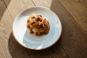 Tempting caramel cinnamon roll topped with pecans on a wooden table, perfect for dessert.