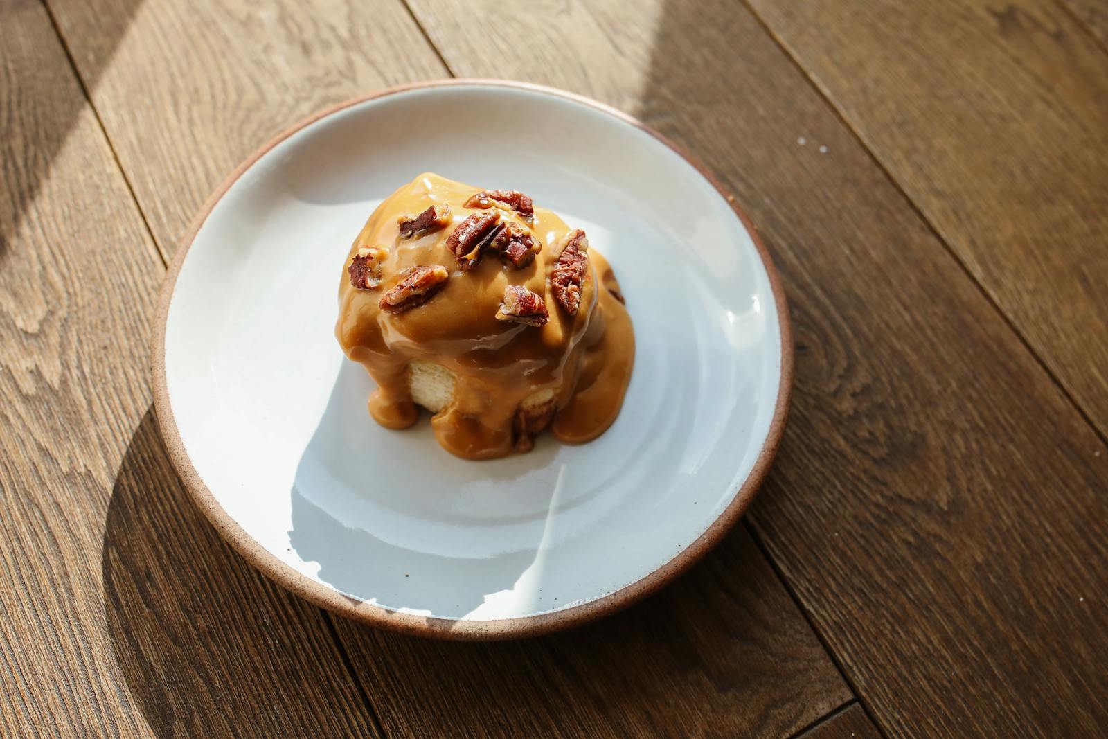 Tempting caramel cinnamon roll topped with pecans on a wooden table, perfect for dessert.