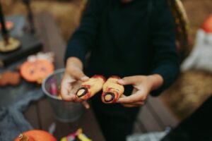 A child holds realistic finger cookies at a Halloween party, spooky and festive.