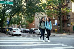 Two friends crossing a city street on a sunny autumn day, enjoying a casual stroll.