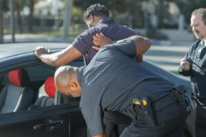 Police officers searching a suspect by a car for public safety and law enforcement.