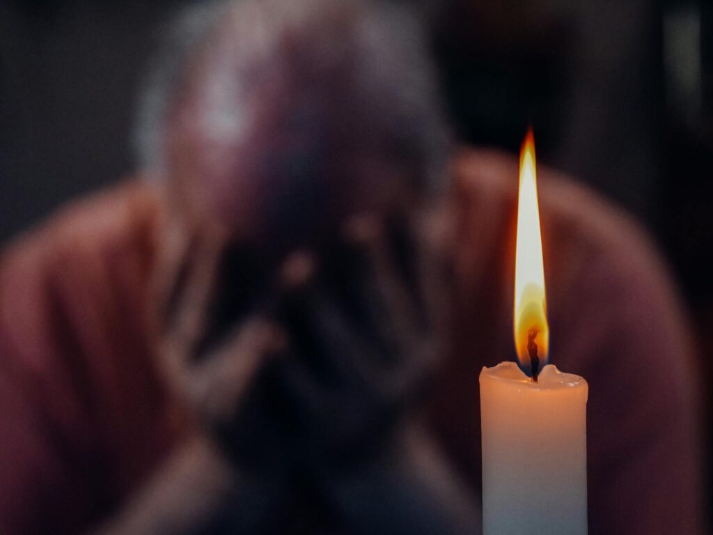 A senior adult in an emotional moment lit by a candle, symbolizing reflection and grief.