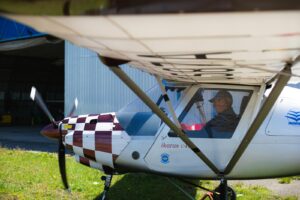 Light aircraft parked near a hangar with a pilot inside ready for takeoff.