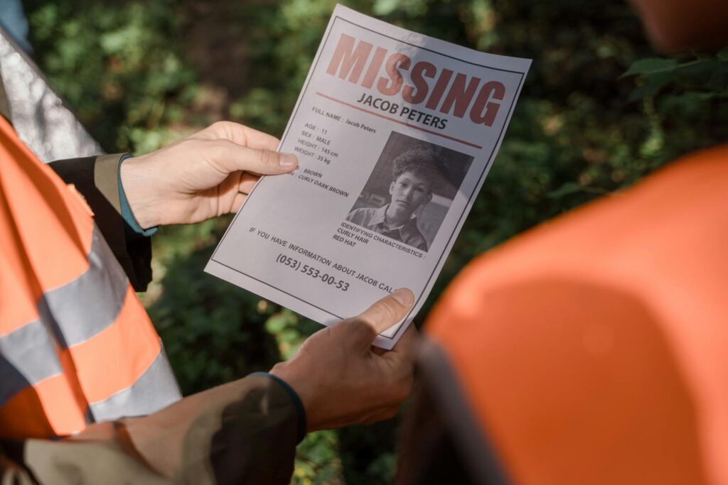 Hands holding a missing person flyer during a search operation in a forest setting, highlighting teamwork and urgency.