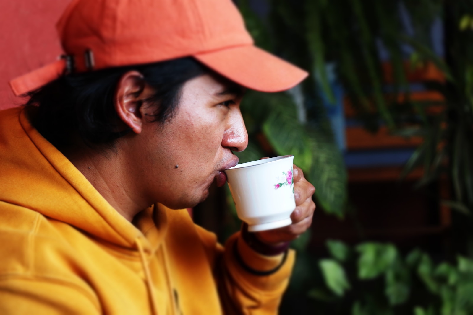 Man in orange cap drinks from white cup.